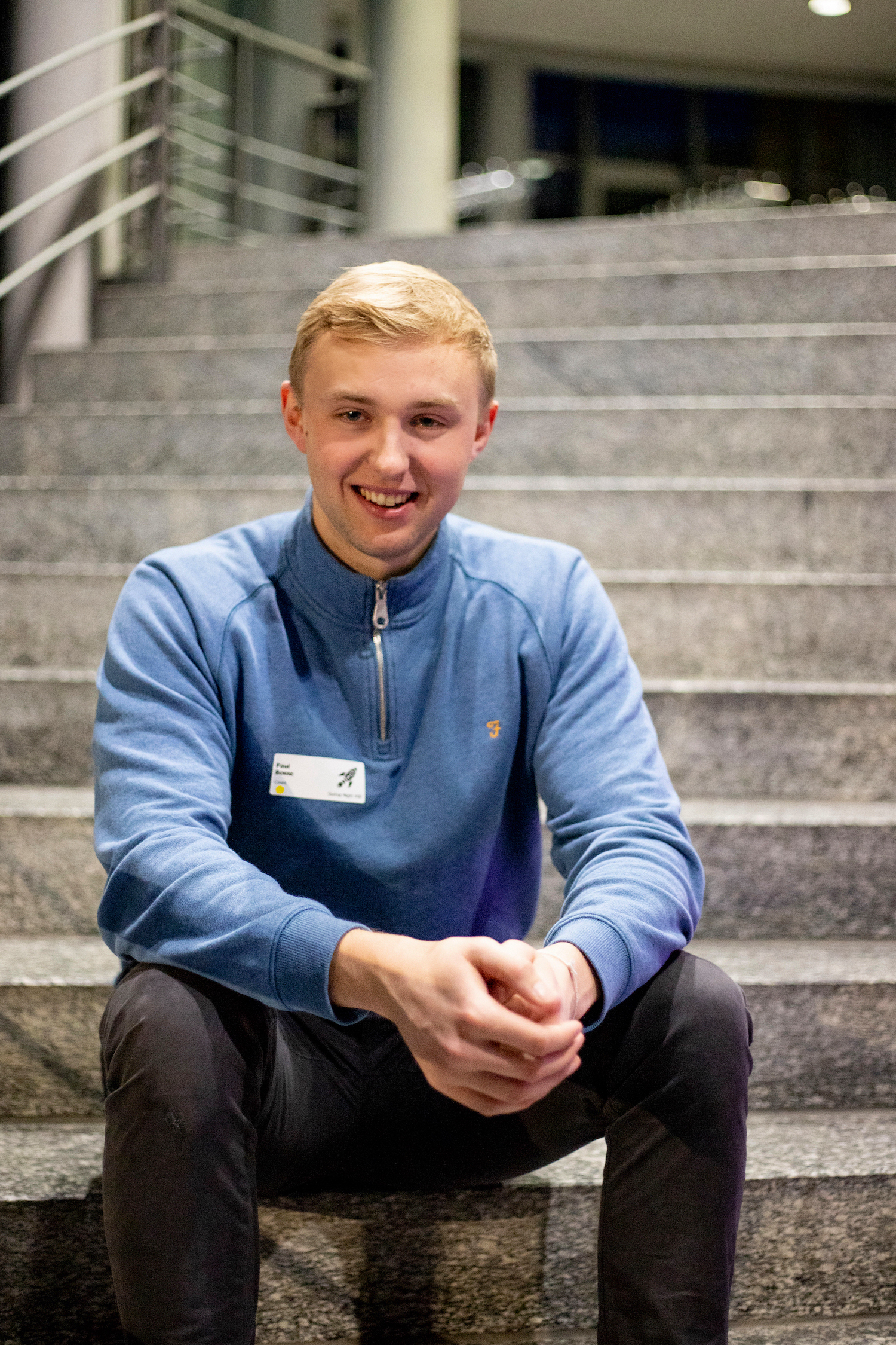 Mann mit hellblonden Haaren und blauem Pulli sitzt auf einer Treppe